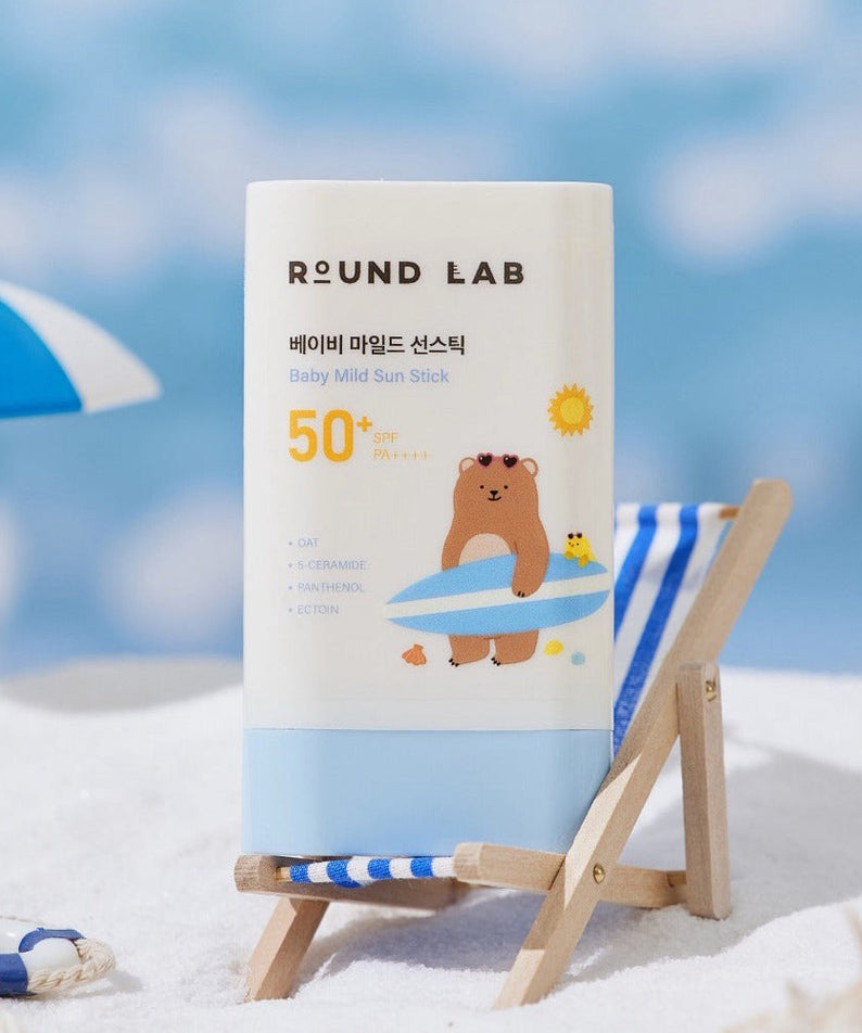 ROUND LAB Baby Mild Sun Stick SPF 50+ PA++++ 21g on a beach chair with a beach umbrella in the background