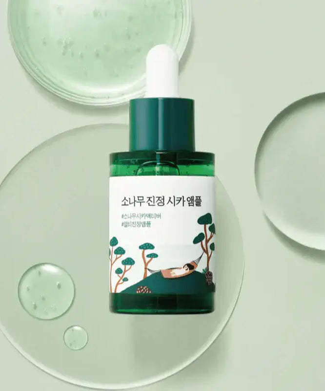 ROUND LAB Pine Calming Cica Ampoule 30ml with green dropper bottle on a light background with liquid droplets.