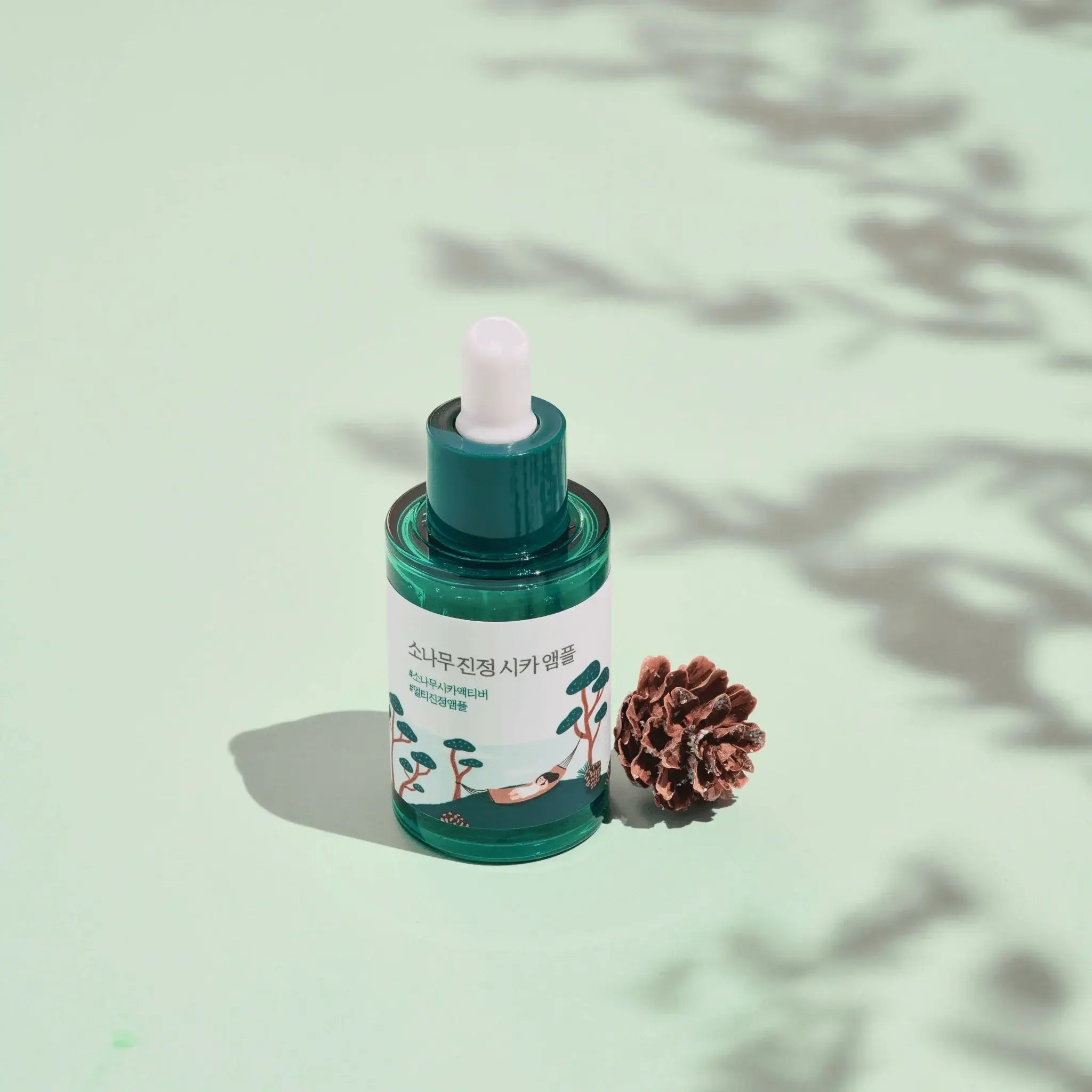 ROUND LAB Pine Calming Cica Ampoule 30ml with pine cone on pastel green background