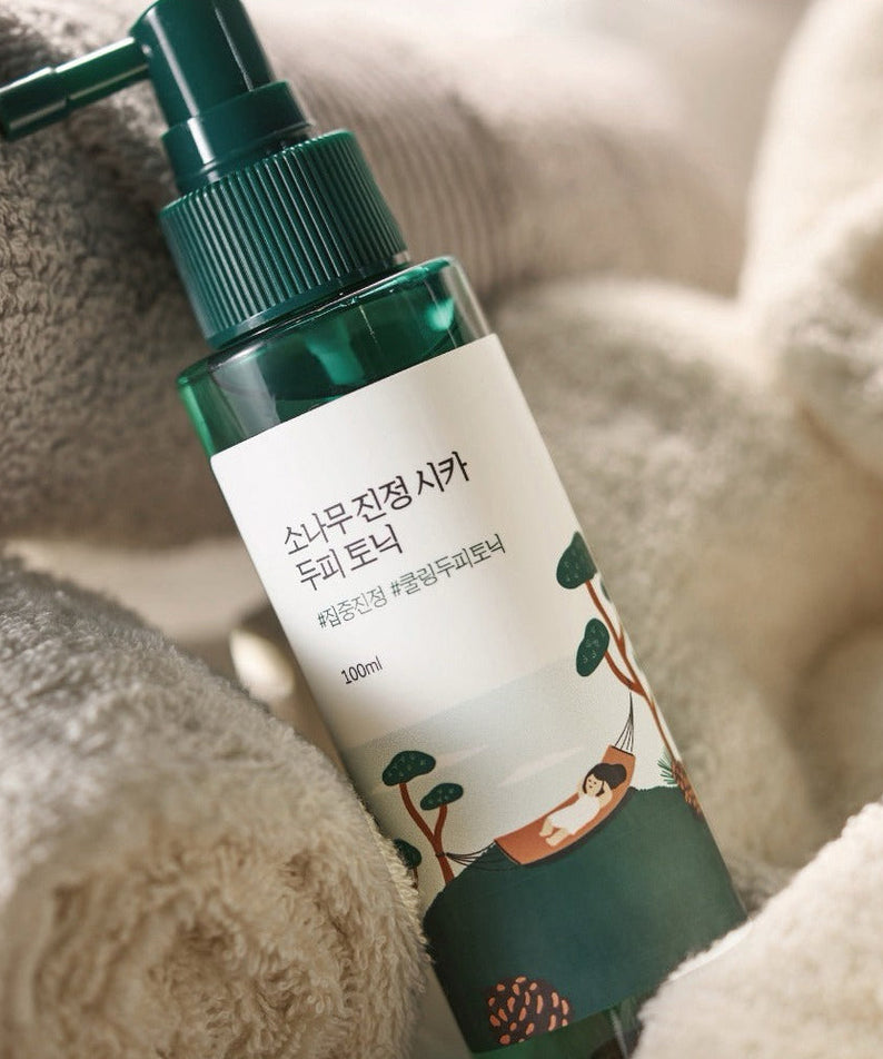 Bottle of ROUND LAB Pine Calming Cica Hair Tonic 100ml with cozy towels.