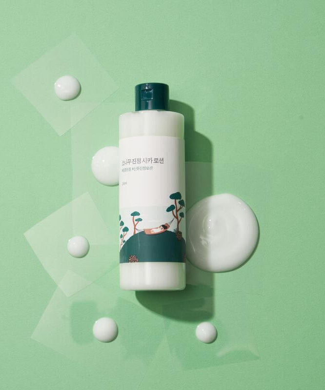 ROUND LAB Pine Calming Cica Lotion 250ml bottle on green background with lotion droplets.