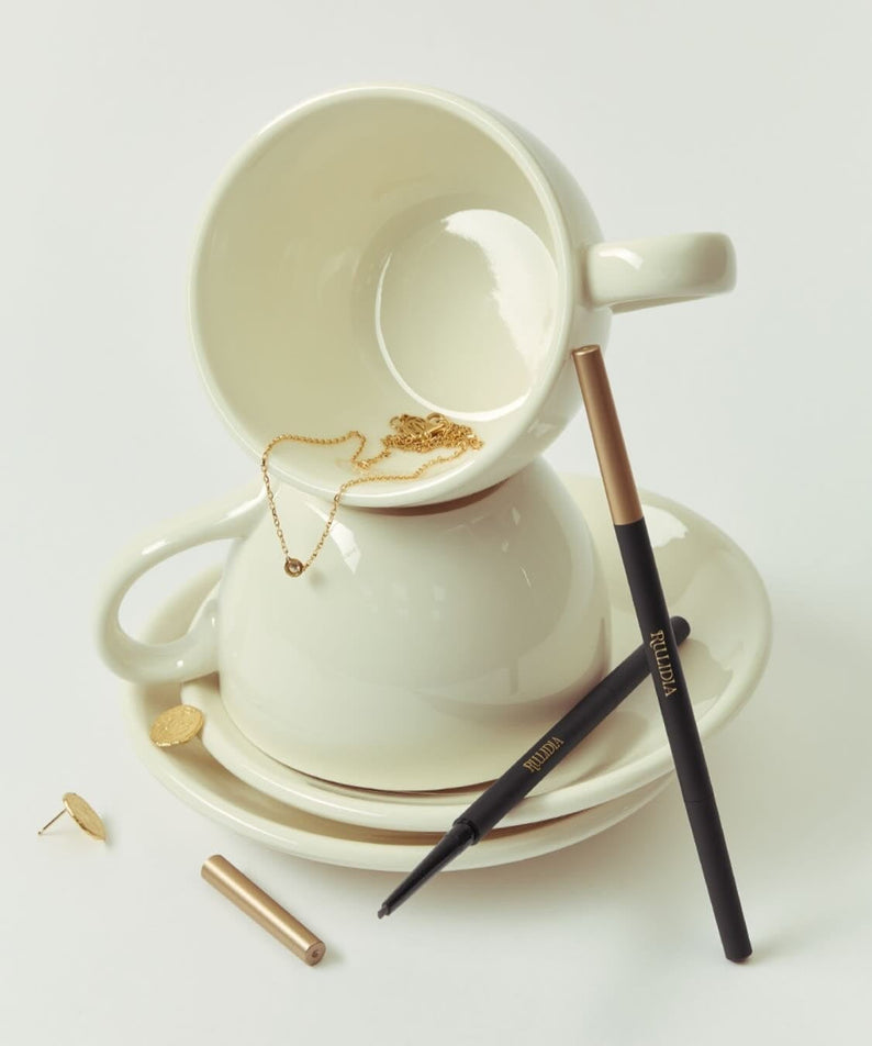 RULIDIA Easy Detail Brow pencil displayed creatively with a ceramic cup and saucer, highlighting its precision and design.