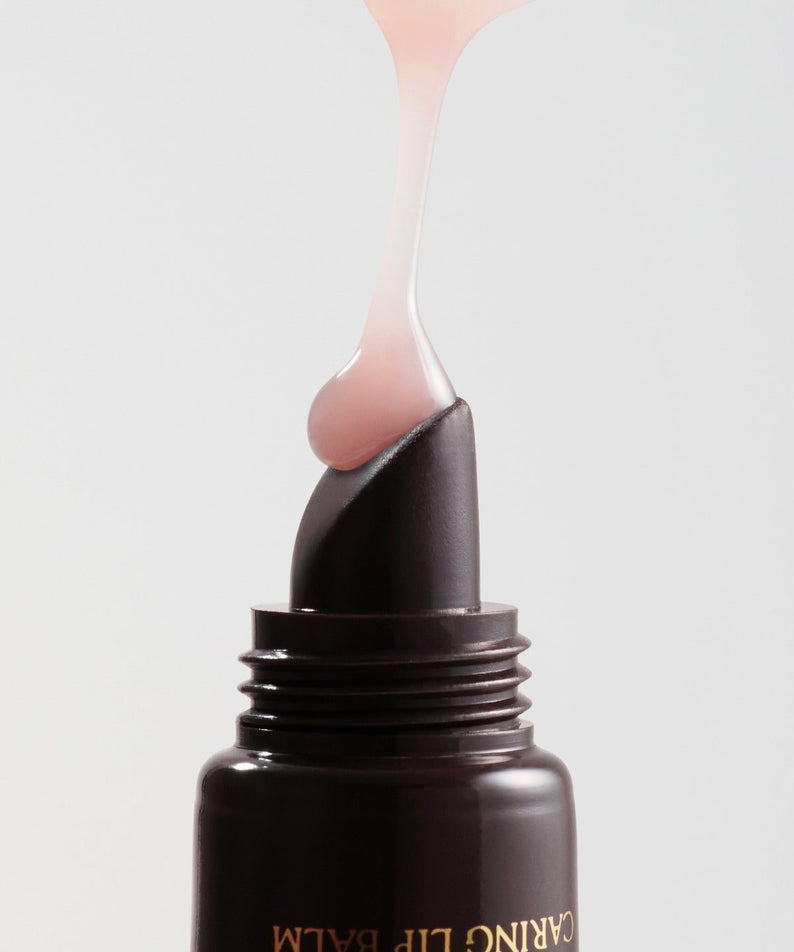 RULIDIA Shining Moment Caring Lip Balm 8g being squeezed from the tube, showcasing its smooth and glossy texture.