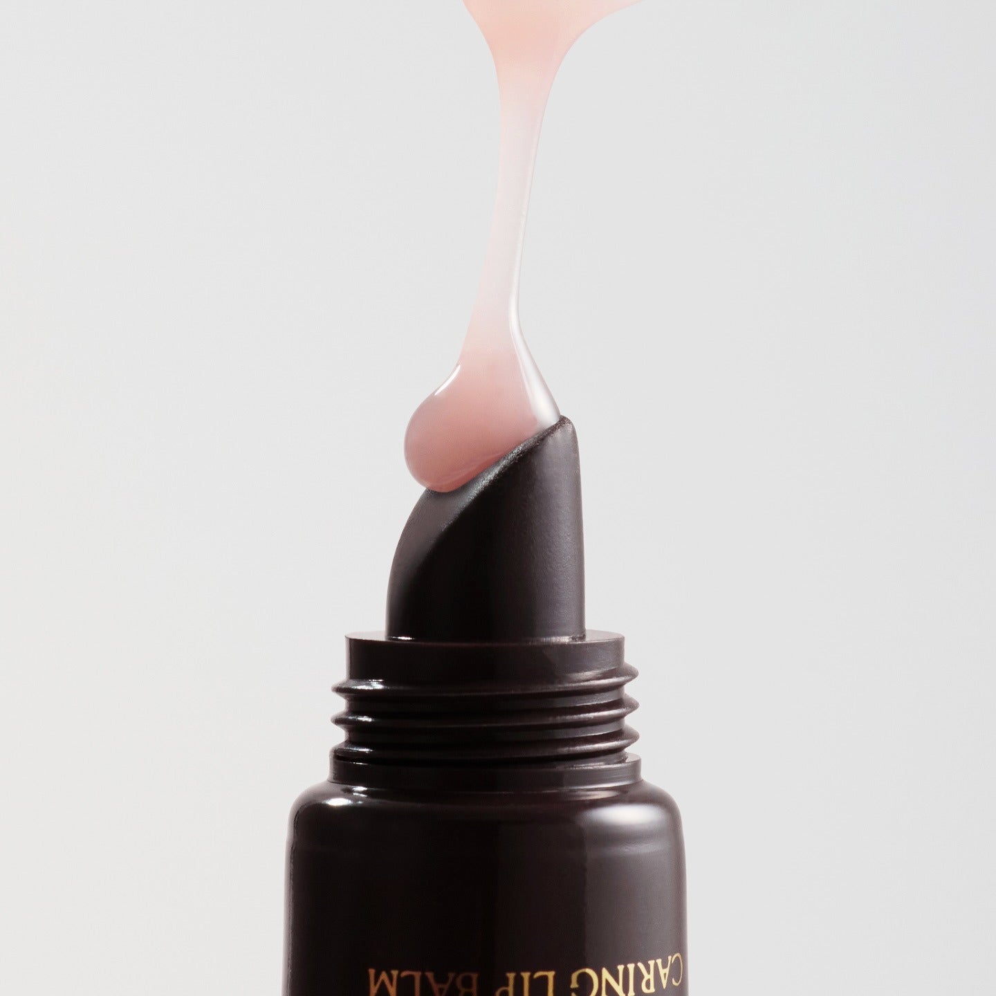 RULIDIA Shining Moment Caring Lip Balm 8g being squeezed from the tube, showcasing its smooth and glossy texture.