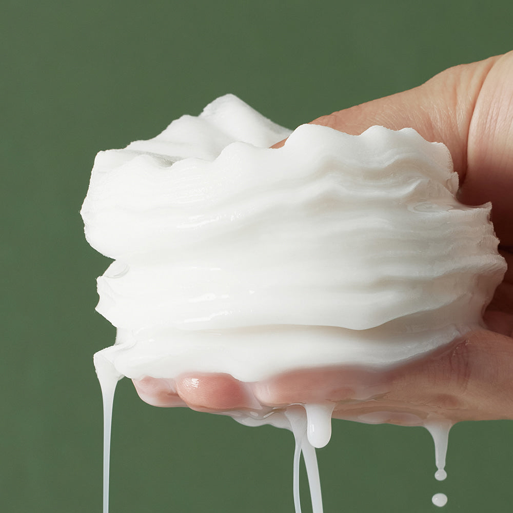 Hand holding layers of moist pads against a green background, depicting texture and consistency of SHAISHAISHAI Repair Milky Skin Peel Pad 60 Pads 120ml.