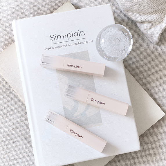 SIM;PLAIN Dewy Volume lip products on a book with clear caps, enhancing a minimalist aesthetic.