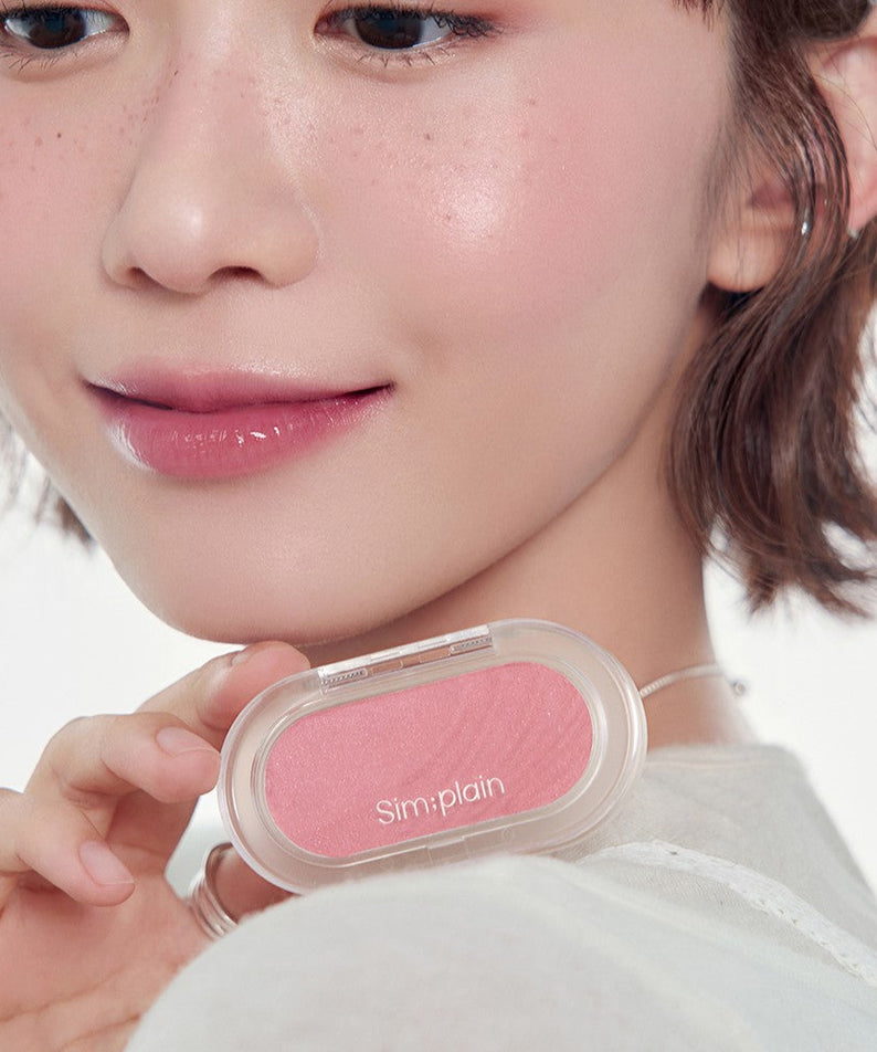 Person holding SIM:PLAIN Gleam On Cheek blush, showcasing rosy cheek effect with the product.