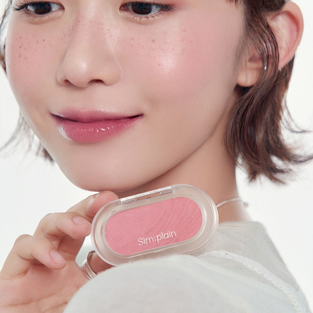 Person holding SIM:PLAIN Gleam On Cheek blush, showcasing rosy cheek effect with the product.