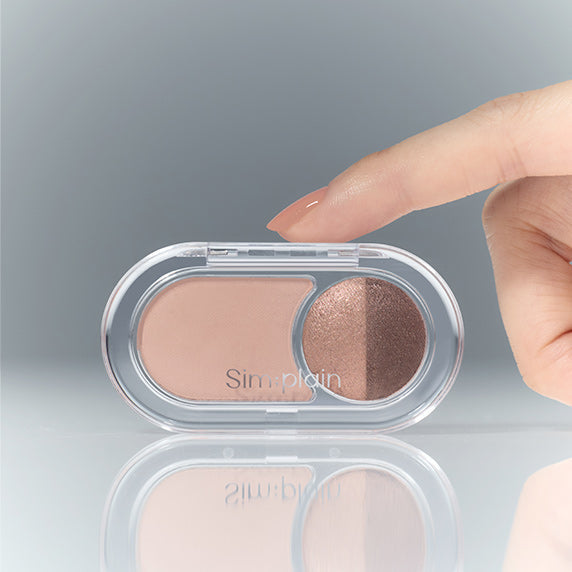 Close-up of a hand reaching for SIM;PLAIN Gleam On Eyes eyeshadow palette featuring two shades.