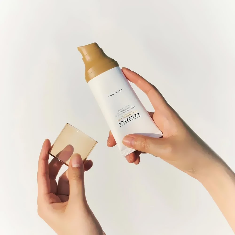 Hands holding SKIN1004 Madagascar Centella Air-fit Sunscreen Light 50ml with cap