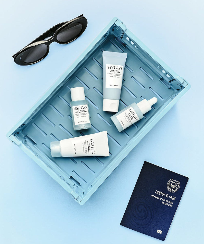 SKIN1004 Madagascar Centella Hyaluronic Acid Travel Kit with skincare products in a blue tray, alongside sunglasses and a passport.