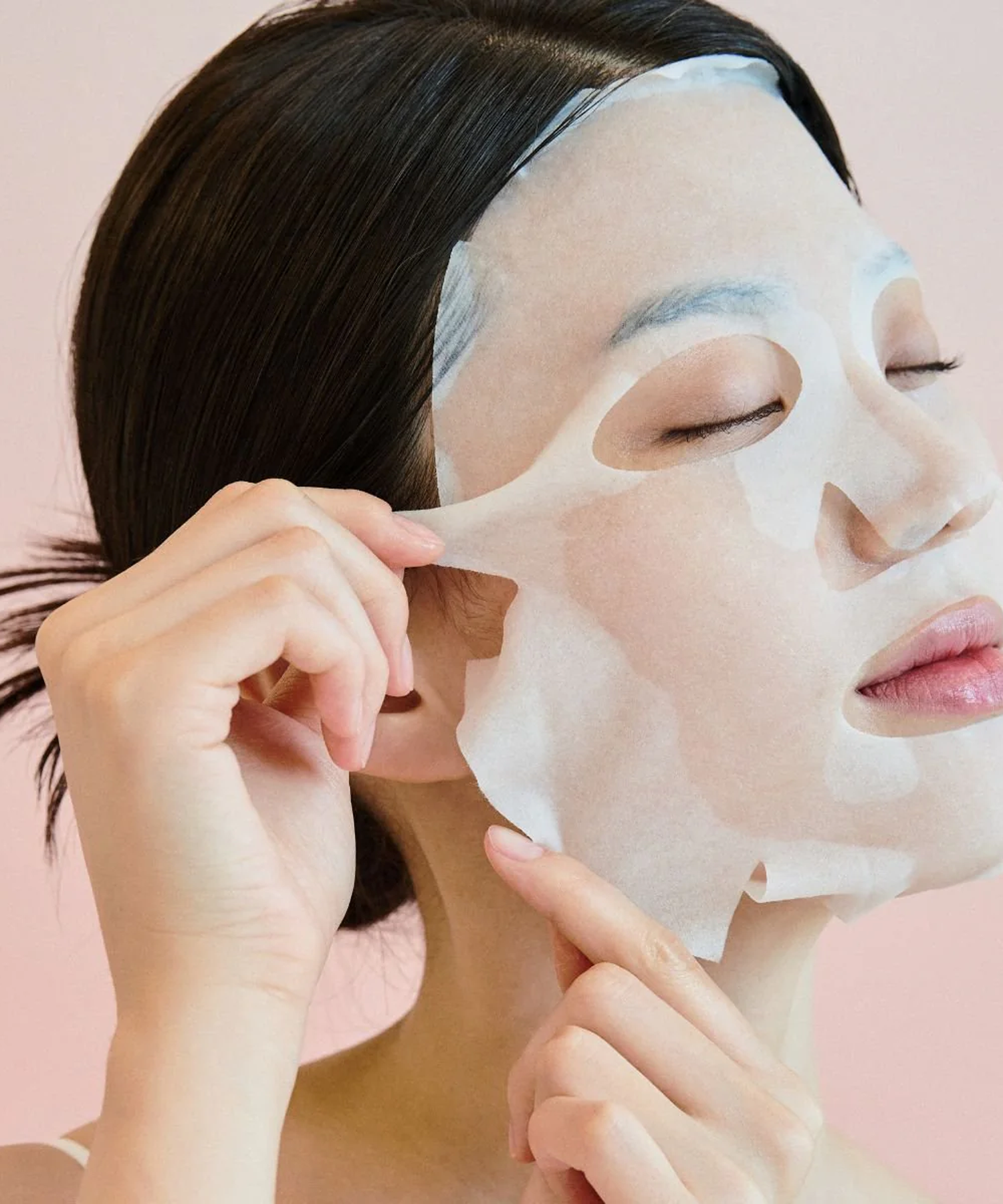 Woman applying SKIN1004 Madagascar Centella Pore-Melting Clarifying Mask 23ml [5 sheets] on a pink background.