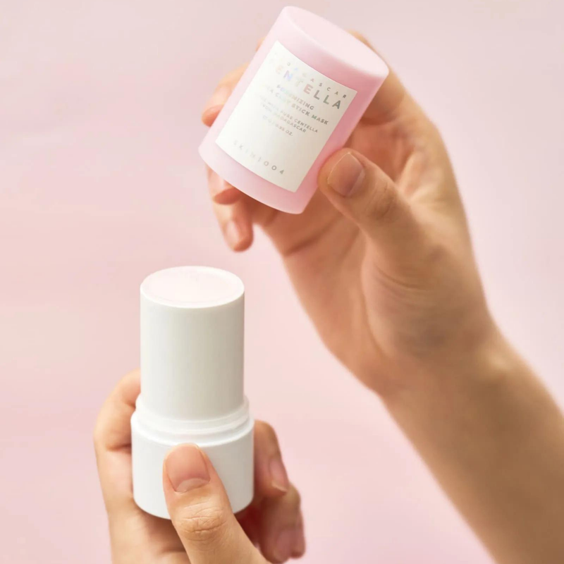 Hands holding SKIN1004 Madagascar Centella Poremising Quick Clay Stick Mask 27g with soft pink background.