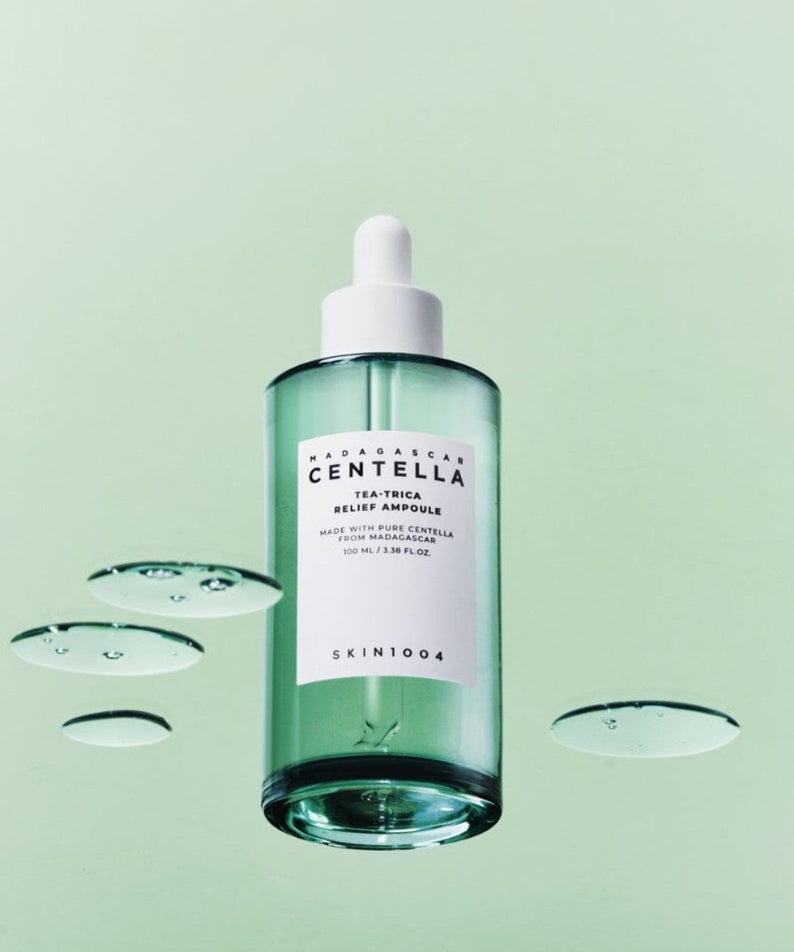 Bottle of SKIN1004 Madagascar Centella Tea-trica Relief Ampoule 100ml with droplets on a green background