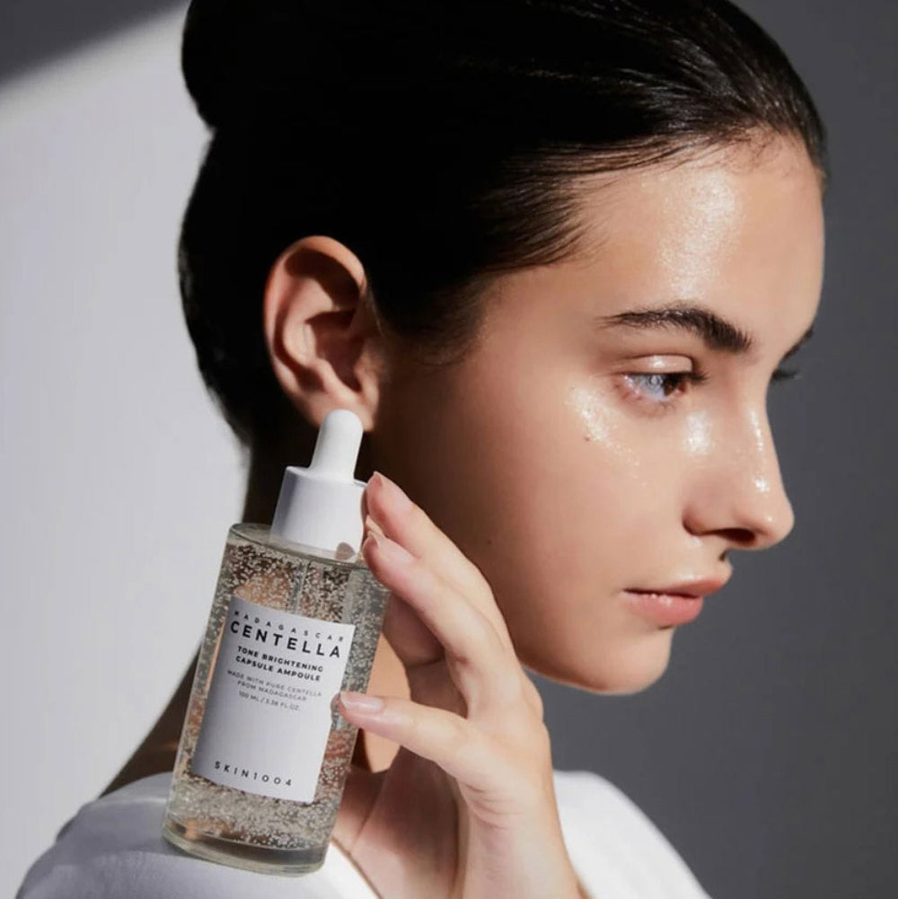 Person holding SKIN1004 Madagascar Centella Tone Brightening Capsule Ampoule 100ml next to face