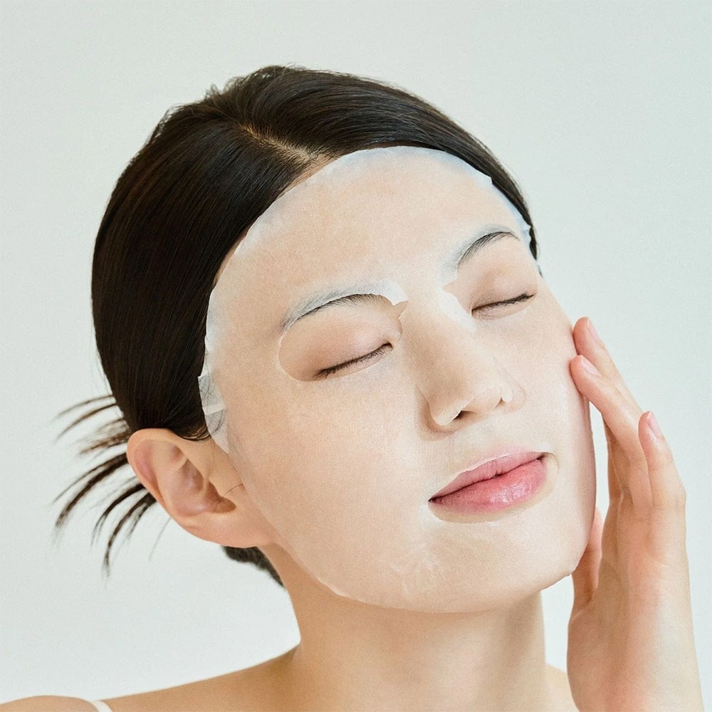 Woman using SKIN1004 Madagascar Centella Tone Brightening Glow Mask 25ml [5 sheets] for radiant skin.