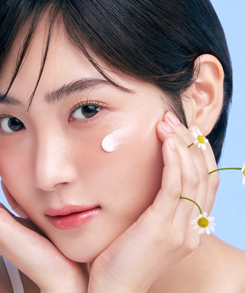 Young woman with smooth skin applying skincare cream, decorated with daisies on fingers.