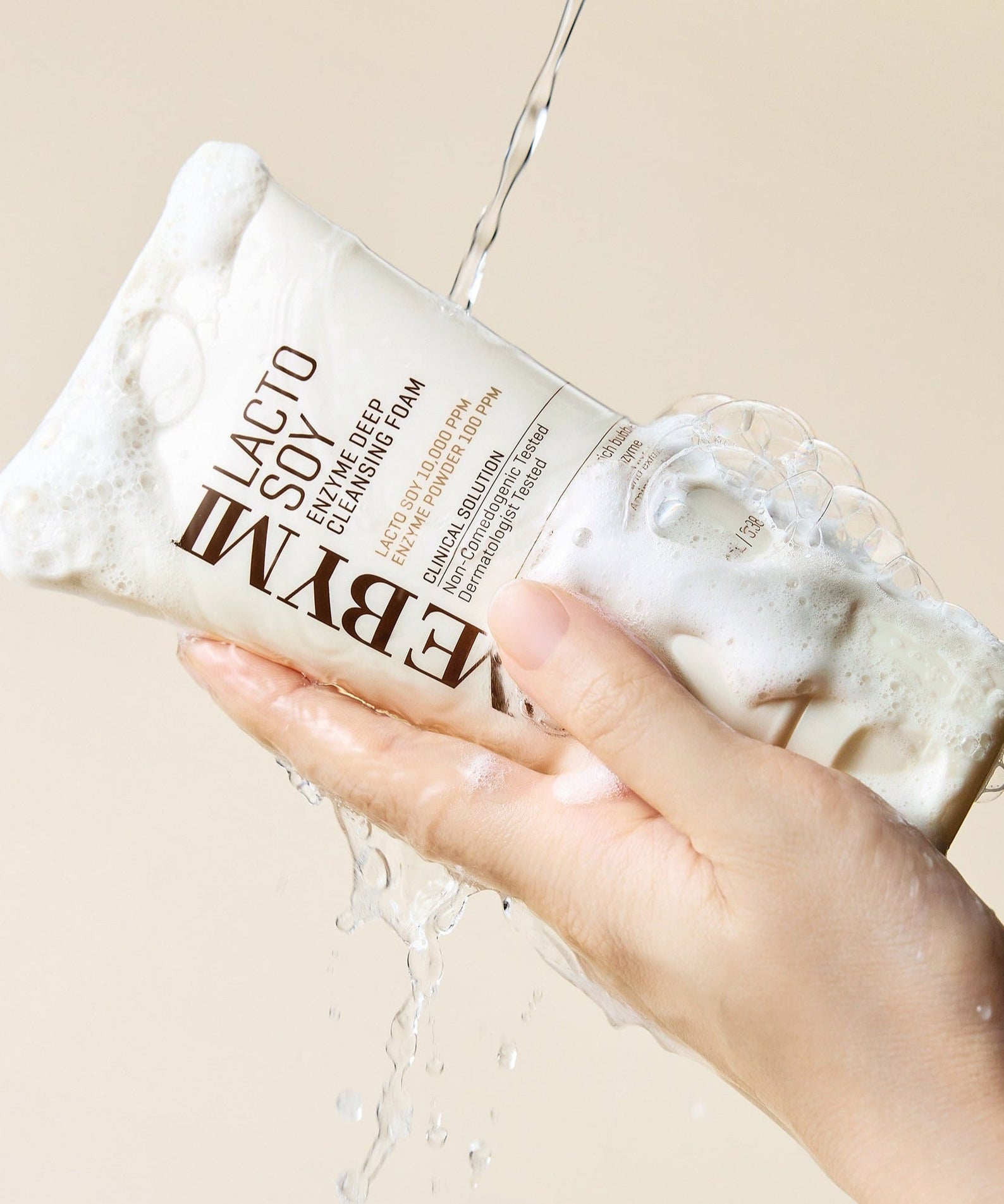 Hand holding SOME BY MI Lactosoy Enzyme Deep Cleansing Foam 100ml with water and bubbles, showcasing cleansing foam texture.