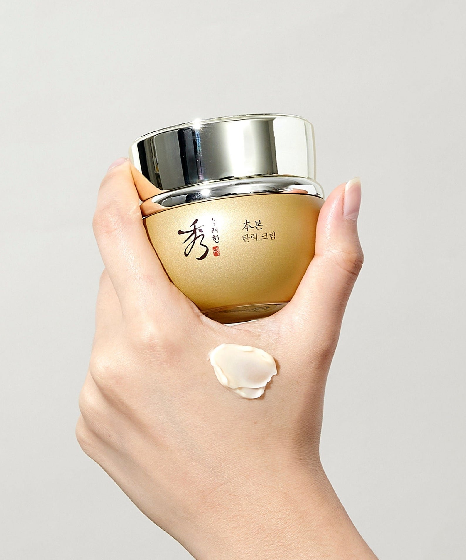 Hand holding SOORYEHAN Bon Elasticity Cream 75ml jar with swatch on skin