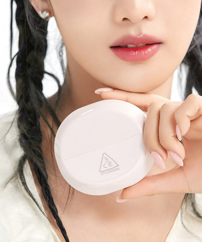 Woman holding STYLE NANDA 3CE Bare Cover Cushion compact close to her face, showcasing product design.