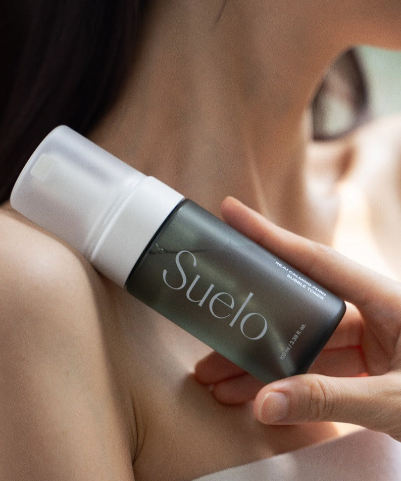Woman holding SUELO Reju Calming PDRN Bubble Toner 100ml bottle against skin, showcasing skincare product