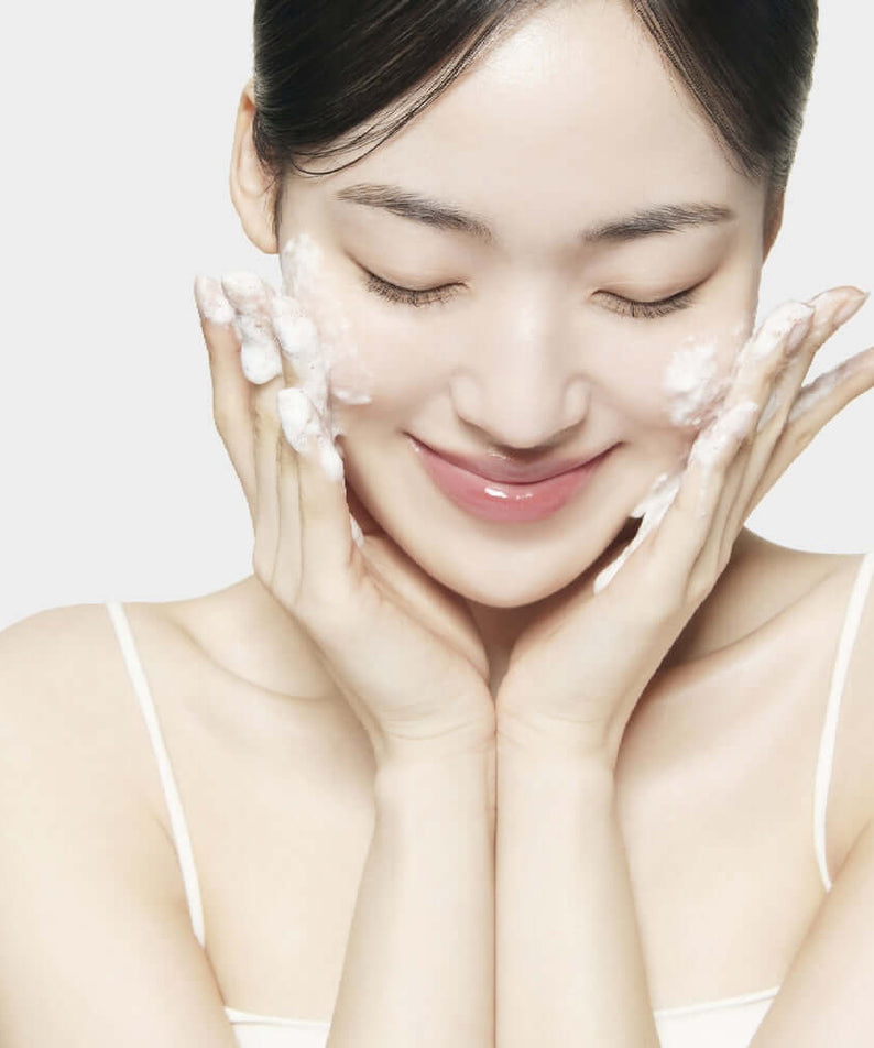 Woman using SU:M37 Secret Rice Nuruk Peeling to Foam Cleanser 120g with gentle bubbles on cheeks, showcasing skincare routine.