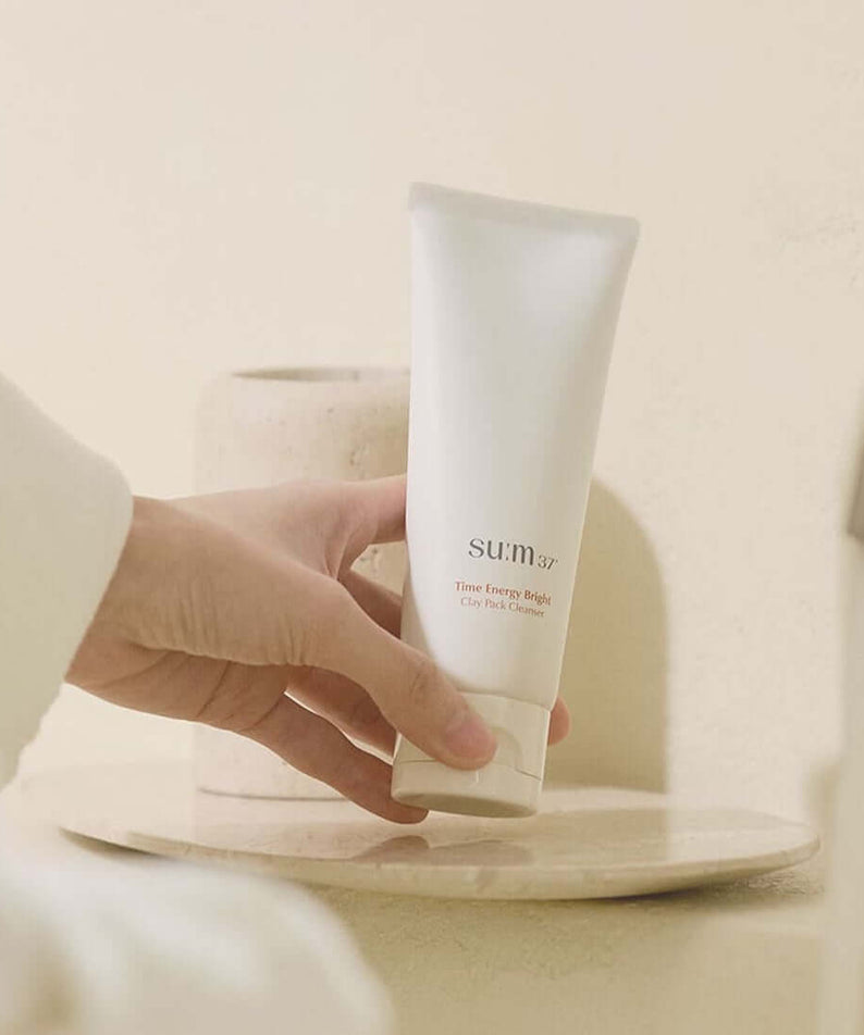 Person holding SU:M37 Time Energy Bright Clay Pack Cleanser 150ml near bathroom sink