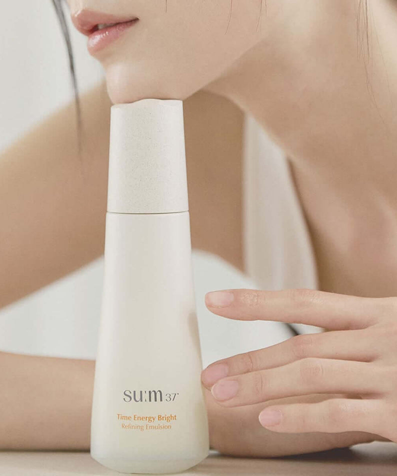 SU:M37 Time Energy Bright Refining Emulsion 120ml displayed next to a model's hand for skincare promotion.