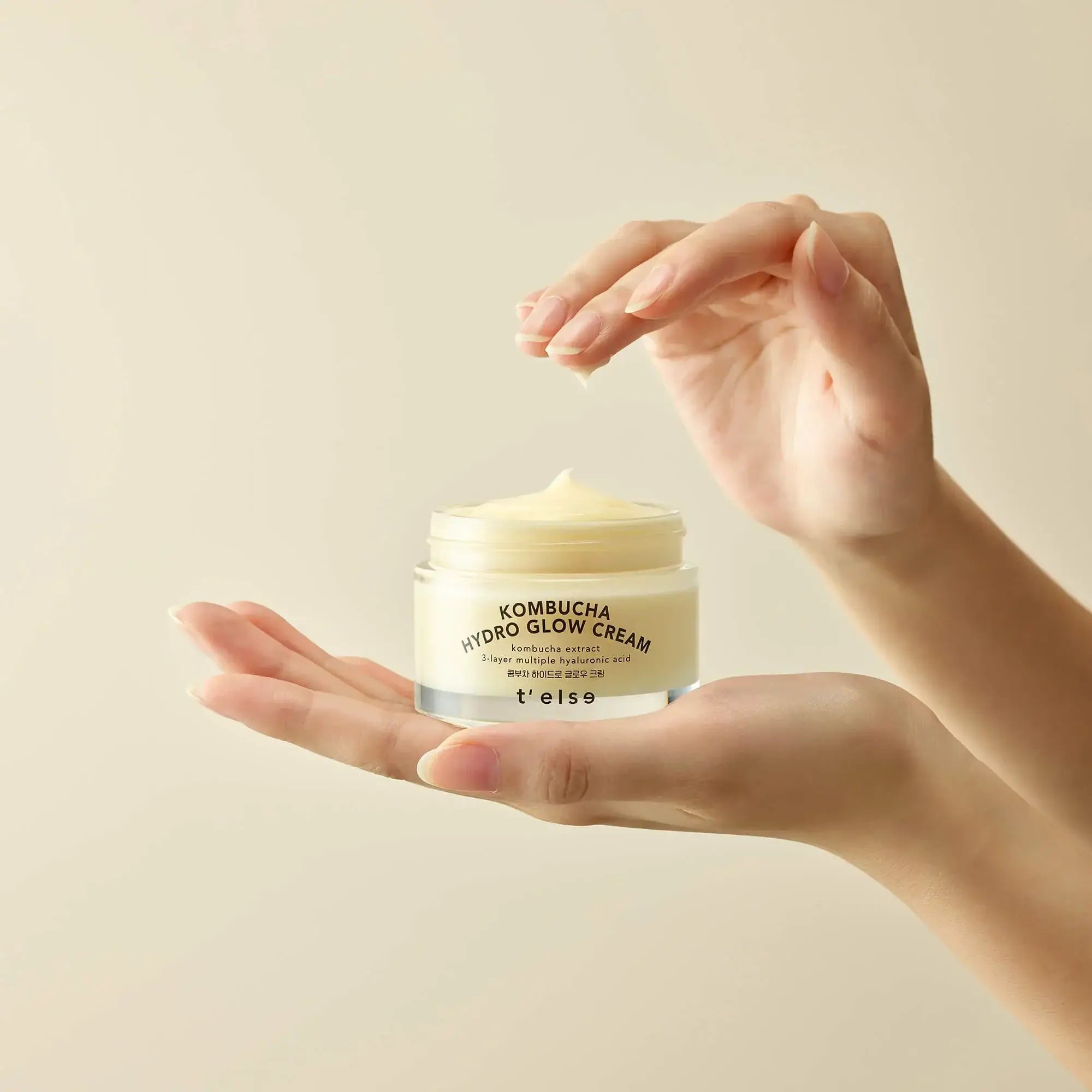 Hands holding T'ELSE Kombucha Hydro Glow Cream 50ml jar against a neutral background