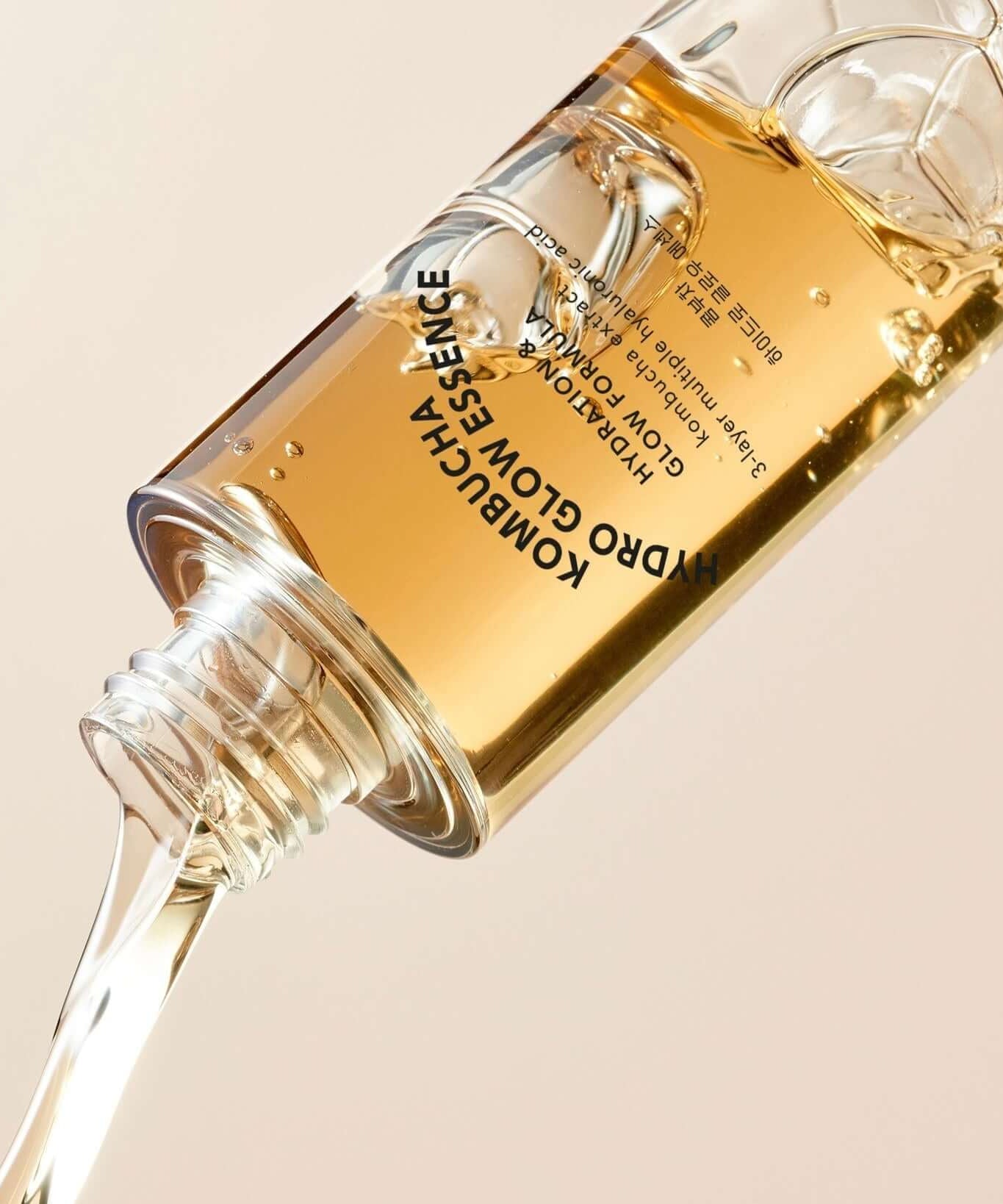 T'ELSE Kombucha Hydro Glow Essence 150ml bottle with liquid pouring out, skincare product in focus on beige background.