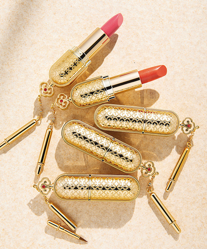 THE WHOO Gong Jin Hyang Mi Luxury Lipstick in royal gold casing with pink and orange shades displayed elegantly on a textured surface