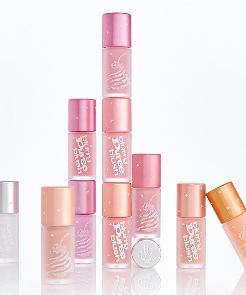 Assorted shades of TIP TOE Blurry Puree Blusher bottles stacked creatively against a white background, showcasing packaging design.