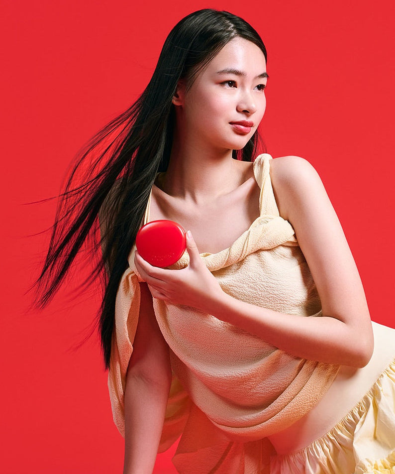 Person holding TOCOBO Apple Dewy Fit Cushion in red packaging against a vibrant red background