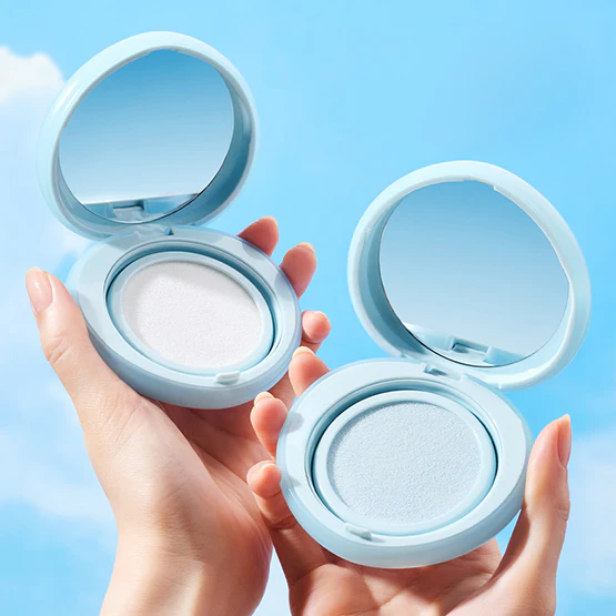 Hands holding TOCOBO Blur Finish Sun Cushion compacts against a blue sky background, showcasing the product's packaging and design.