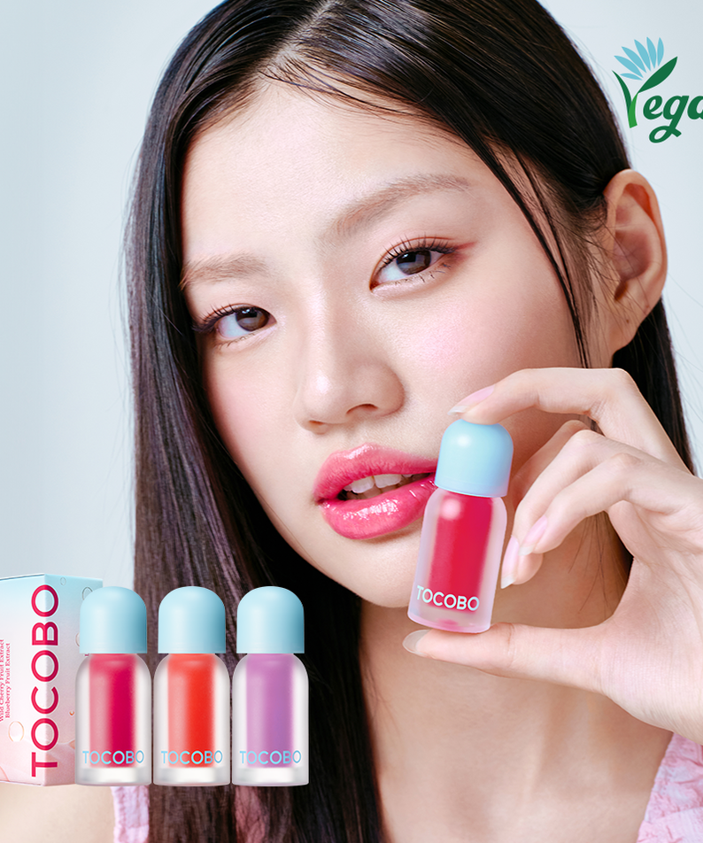 Model holding TOCOBO Juicy Berry Pluming Lip Oil next to lip oil bottles and vegan logo.