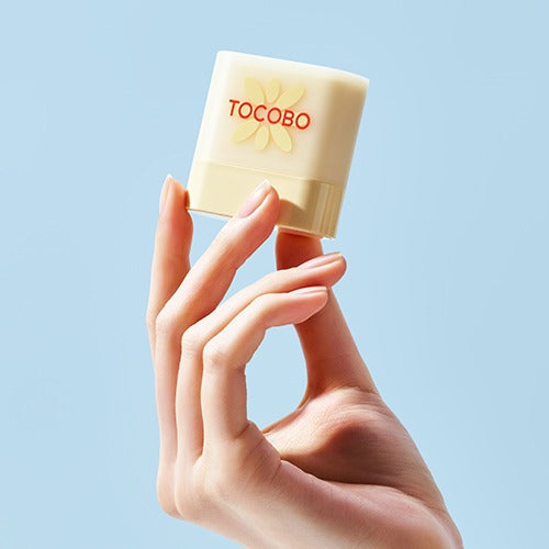 Hand holding a TOCOBO Mini Sun Stick Trio against a blue background