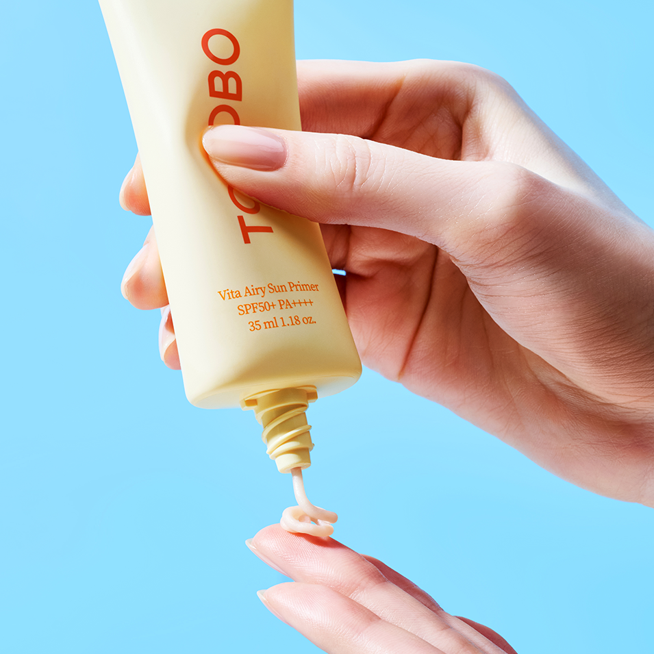 Applying TOCOBO Vita Airy Sun Primer 35ml on hand with blue background for skincare routine