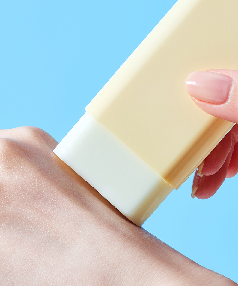 Applying TOCOBO Vita Waterproof Sun Stick on skin with a blue background.