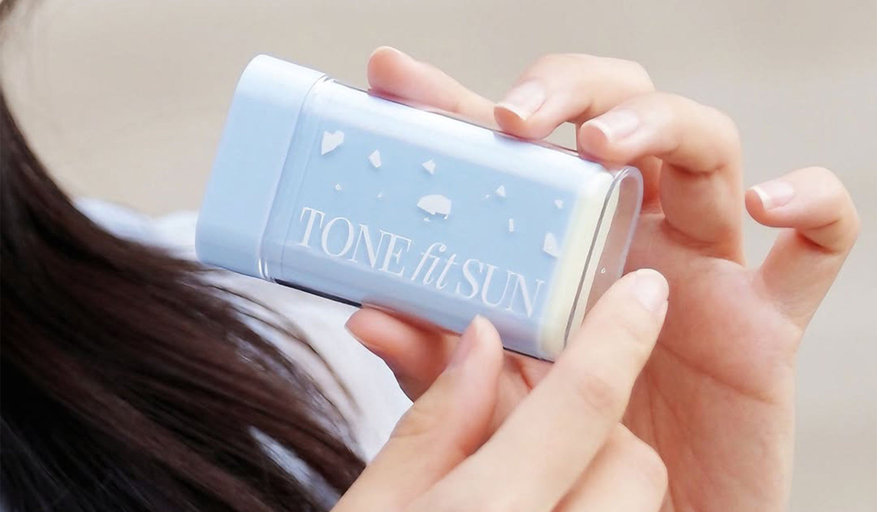 Person holding Tone Fit Sun stick, showcasing sun protection skincare product.