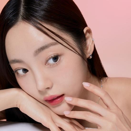 Woman with dewy skin and subtle makeup, gently holding her face against a pastel pink background. Skincare beauty concept.