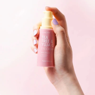 Hand holding TONYMOLY Pure Dew Tea Tree & Yuzu Seed Vitality Eye Cream 30ml against a pink background.