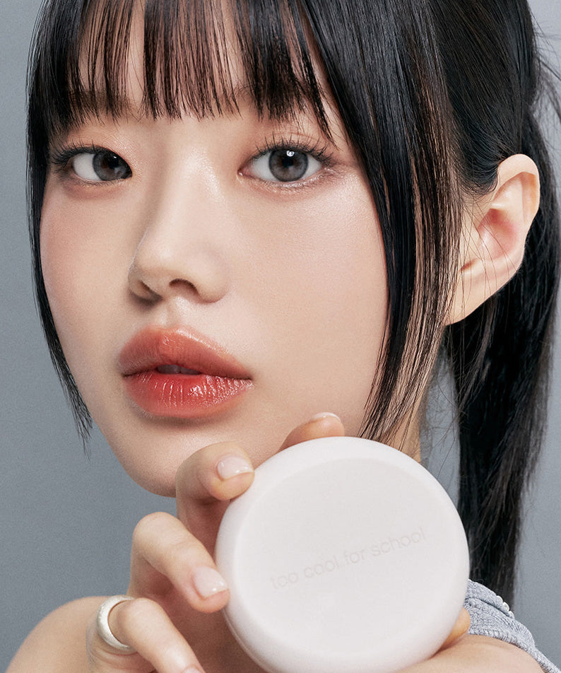 Model holding TOO COOL FOR SCHOOL Fixing Nude Fit Cushion [Product + Refill] showing product design and texture.