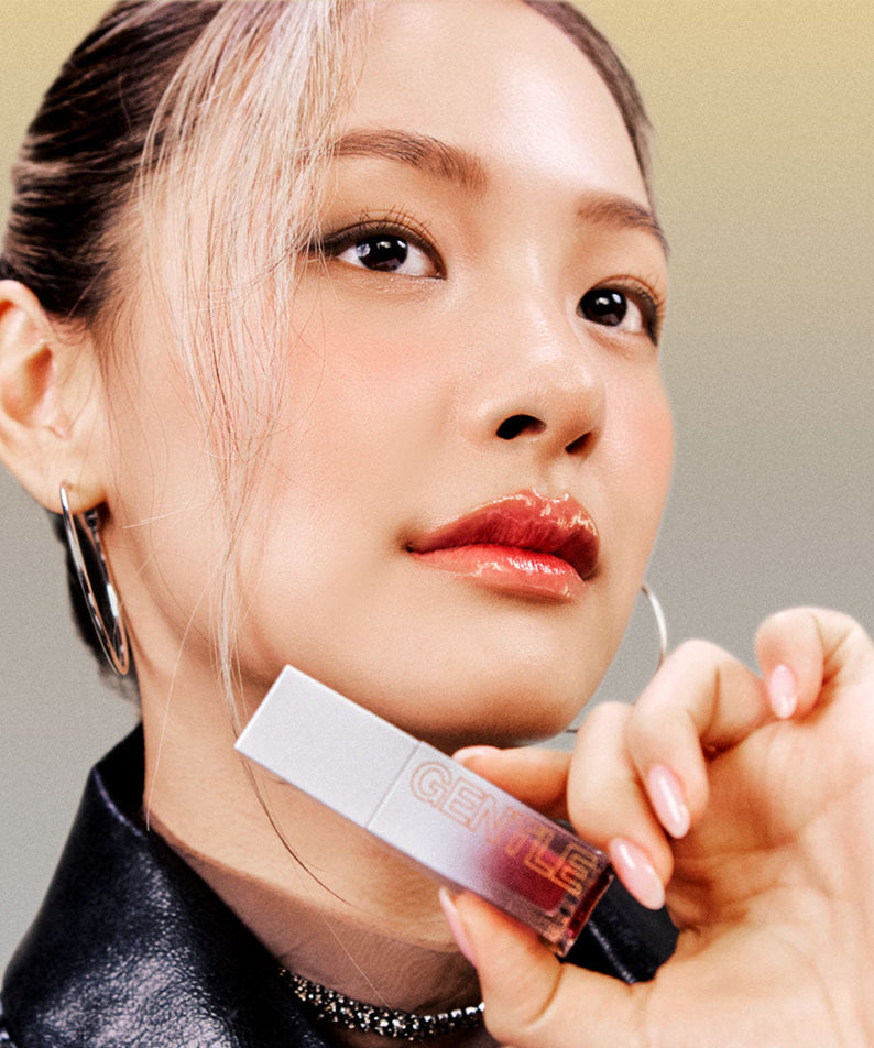 Model holding TOOQ Gentle Kiss Glow Tint with shimmering lip finish