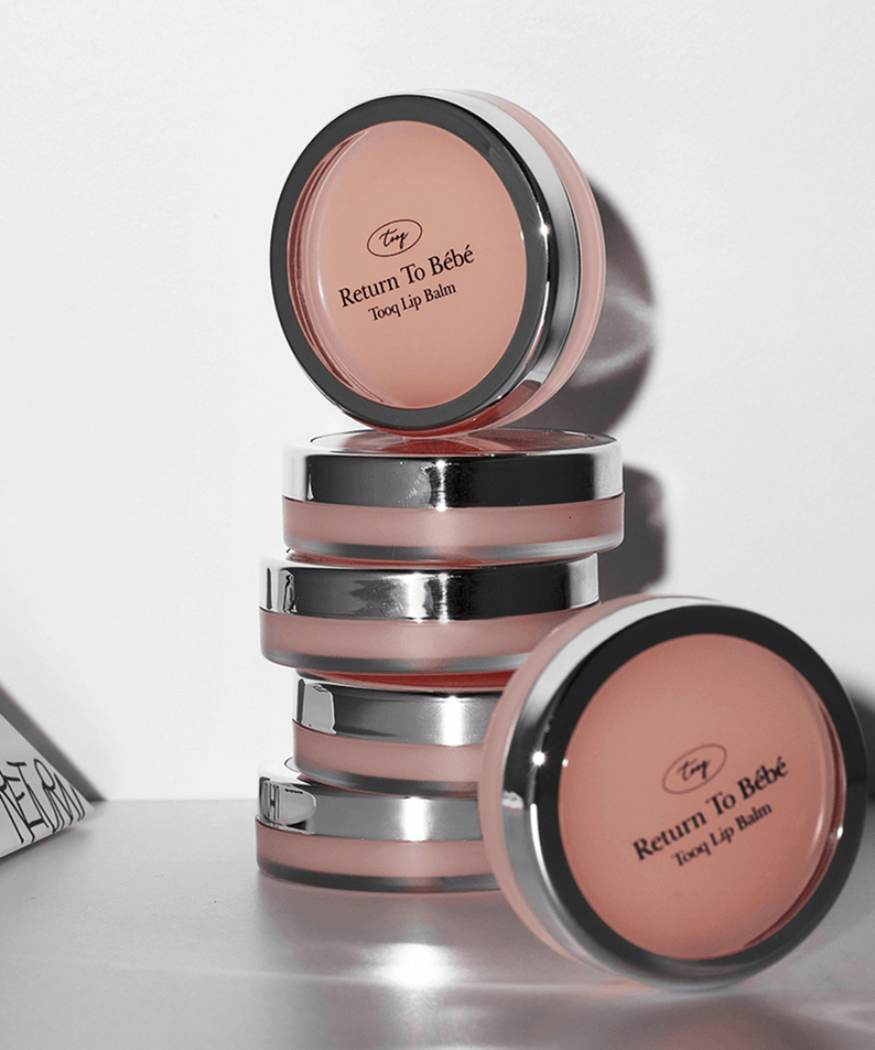 Stack of TOOQ Return To BÃ¨bÃ¨ Lip Balm containers with pink tint and sleek design.