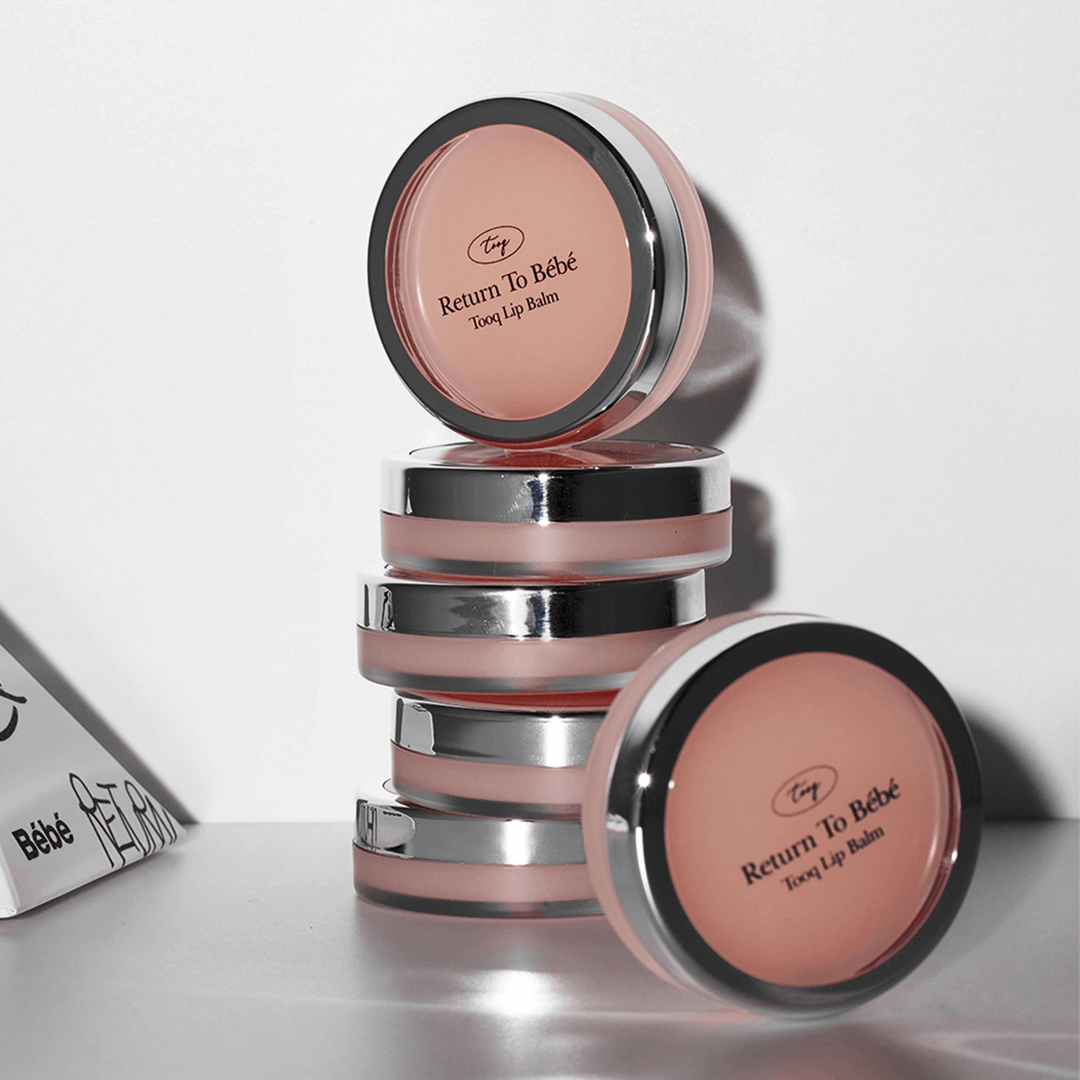 Stack of TOOQ Return To BÃ¨bÃ¨ Lip Balm containers with pink tint and sleek design.
