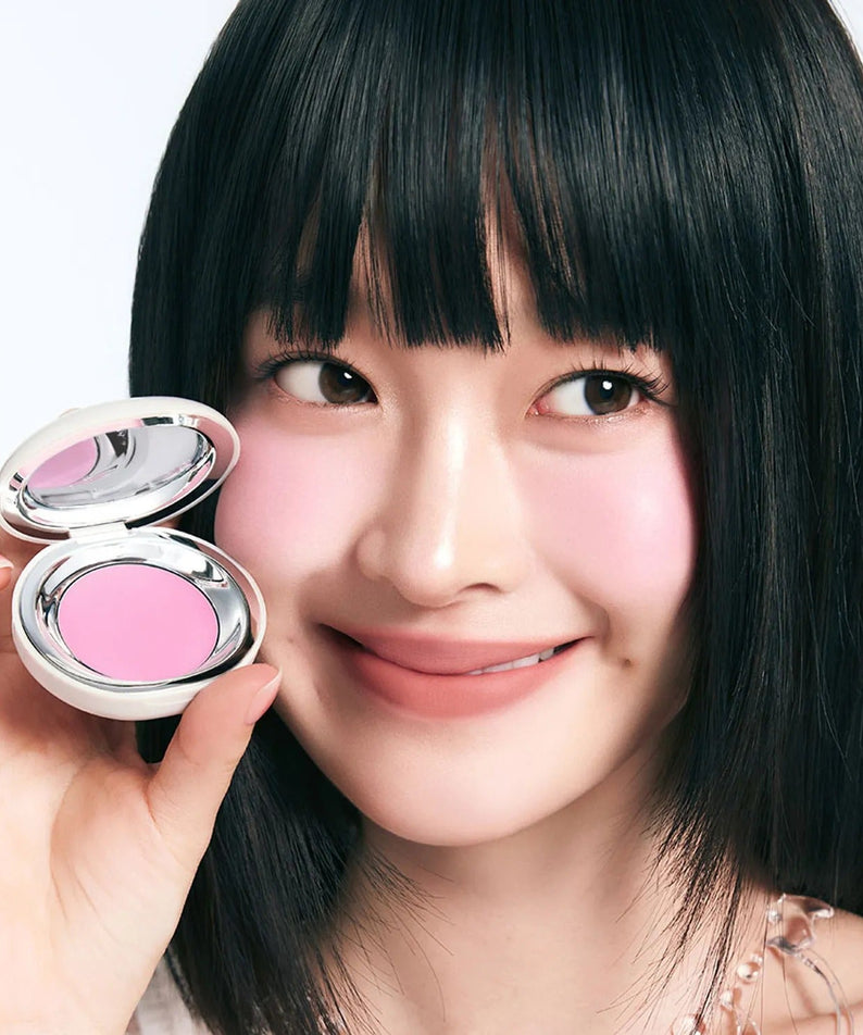 Model applying TOOQ Satin Peach Blossom blush with a smile.