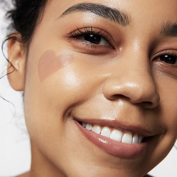 Smiling woman with TOUCH IN SOL Pretty Filter In My Heart Stick Foundation heart shape on cheek, showcasing natural glow.