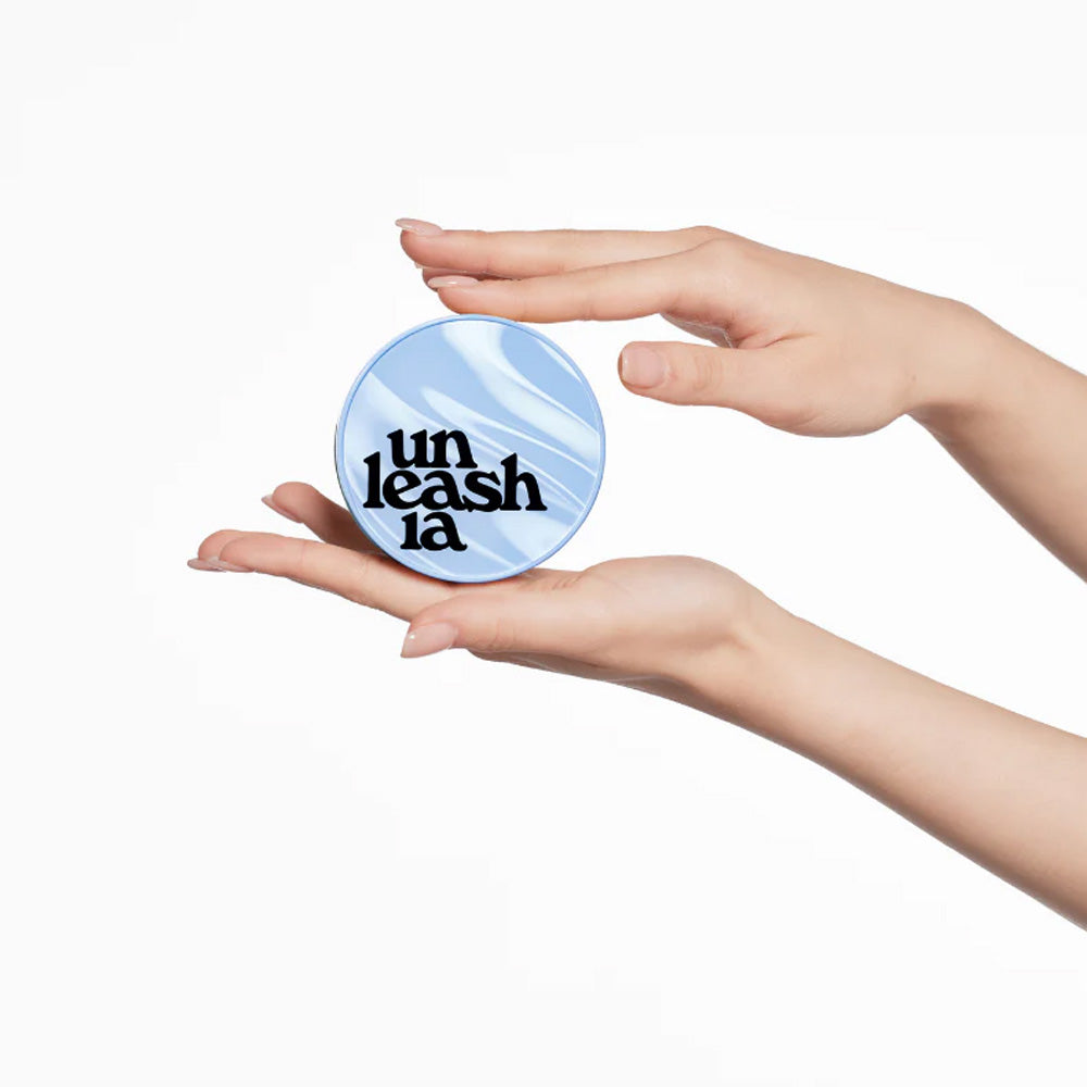 Hands holding UNLEASHIA Babe Skin Baby Blue Cushion compact makeup product with stylish packaging.