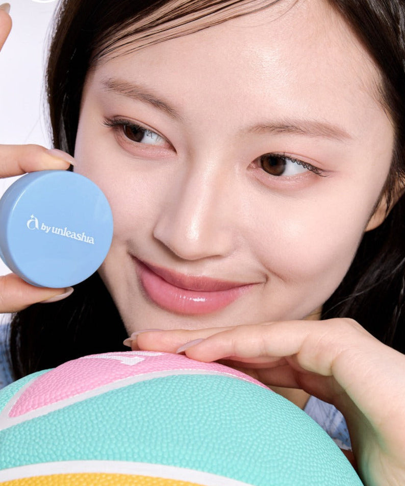 Smiling woman holding UNLEASHIA Be Be Blue Cushion beside her face, demonstrating smooth coverage and radiant skin