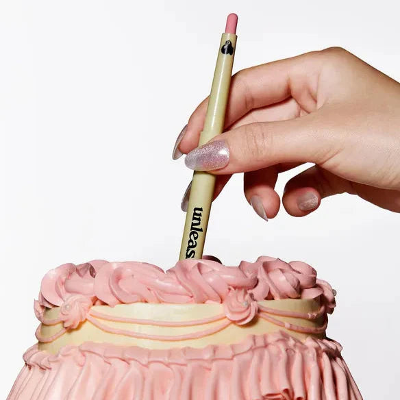 UNLEASHIA Oh! Happy Day Lip Pencil being held above a pink cake with intricate icing details.